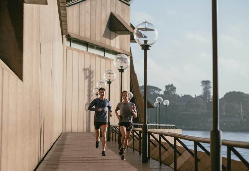 Two people jogging by the Sydney Opera House on a sunny day, capturing a healthy lifestyle.