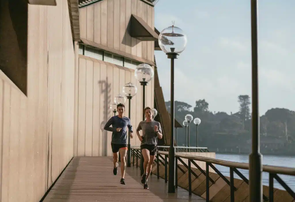 Two people jogging by the Sydney Opera House on a sunny day, capturing a healthy lifestyle.